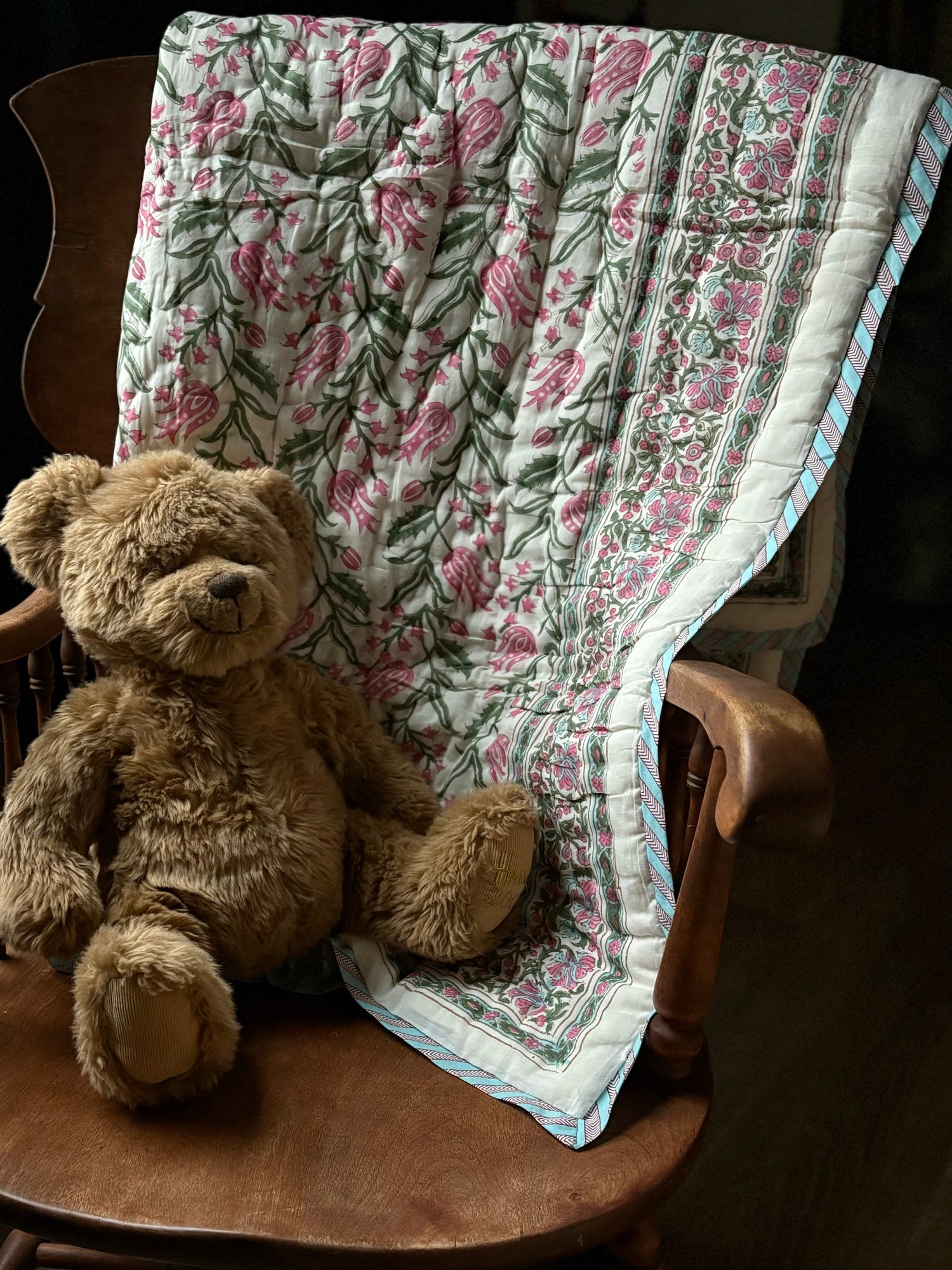 Beautiful floral quilt draped over rocking chair with fuzzy brown teddy bear